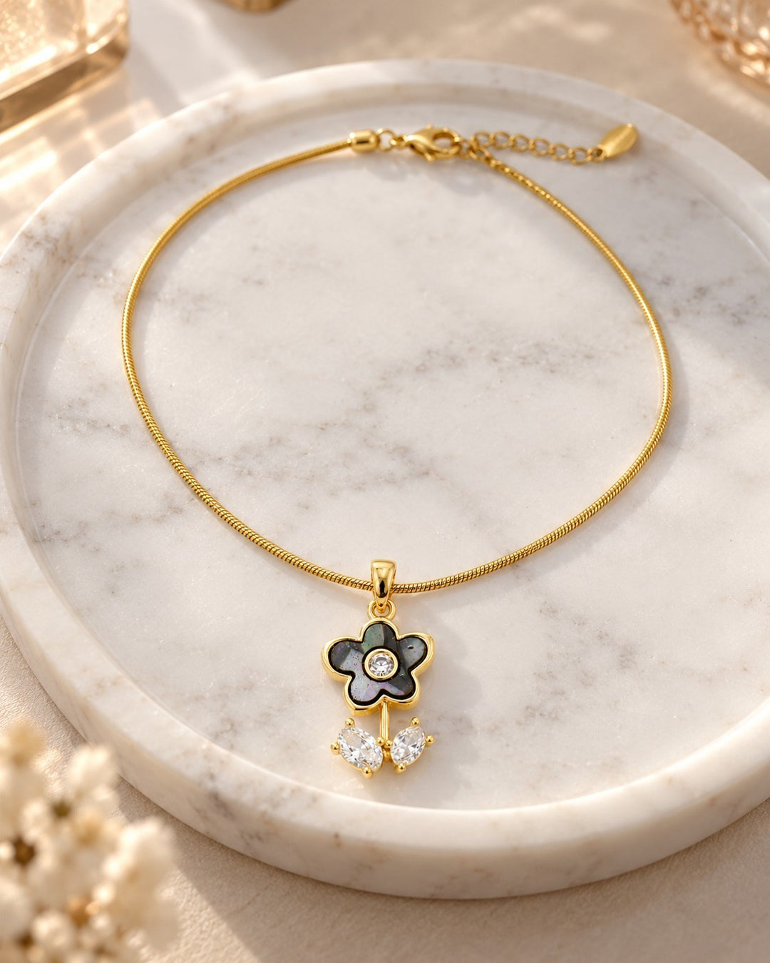 Elli Jewellery gold plated snake chain necklace with a black floral pendant and sparkling cubic zirconia on marble