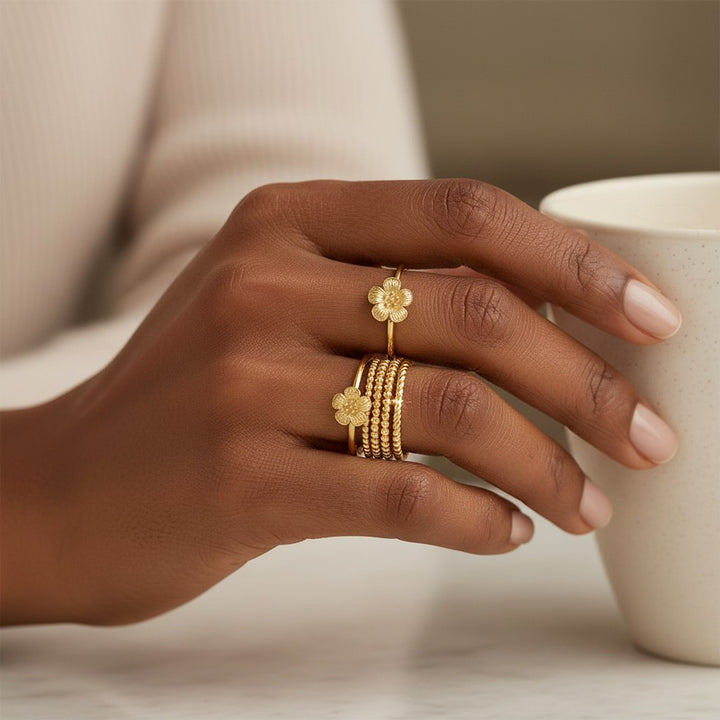 Elli Jewellery 3-piece gold plated flower ring set worn on a woman's hand holding a white ceramic mug.