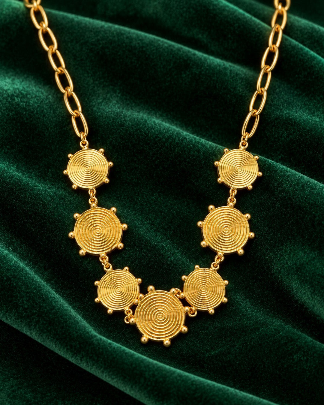 Elli Jewellery gold plated waterproof necklace featuring geometric spiral circle links on a dark green velvet background