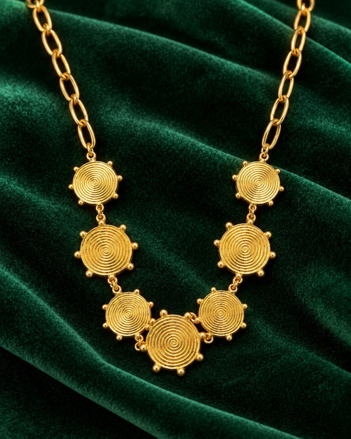 Elli Jewellery gold plated waterproof necklace featuring geometric spiral circle links on a dark green velvet background