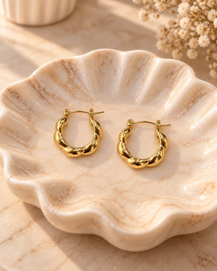 Elli Jewellery gold plated chunky geometric hoop earrings resting in a decorative scalloped ceramic dish.
