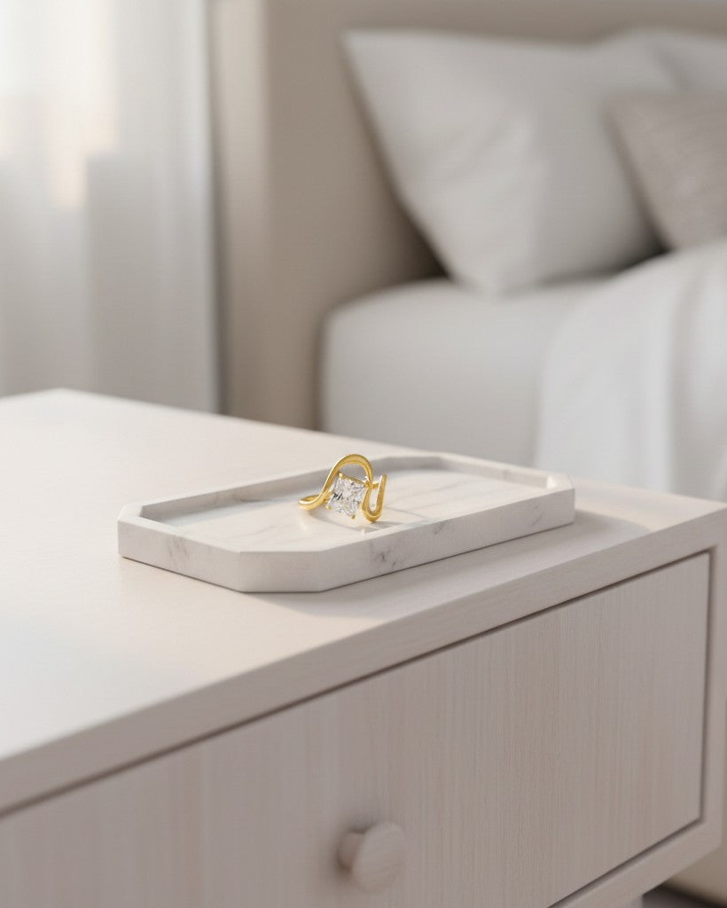 Elli Jewellery gold plated geometric ring with a clear stone on a white marble tray in a bedroom setting.