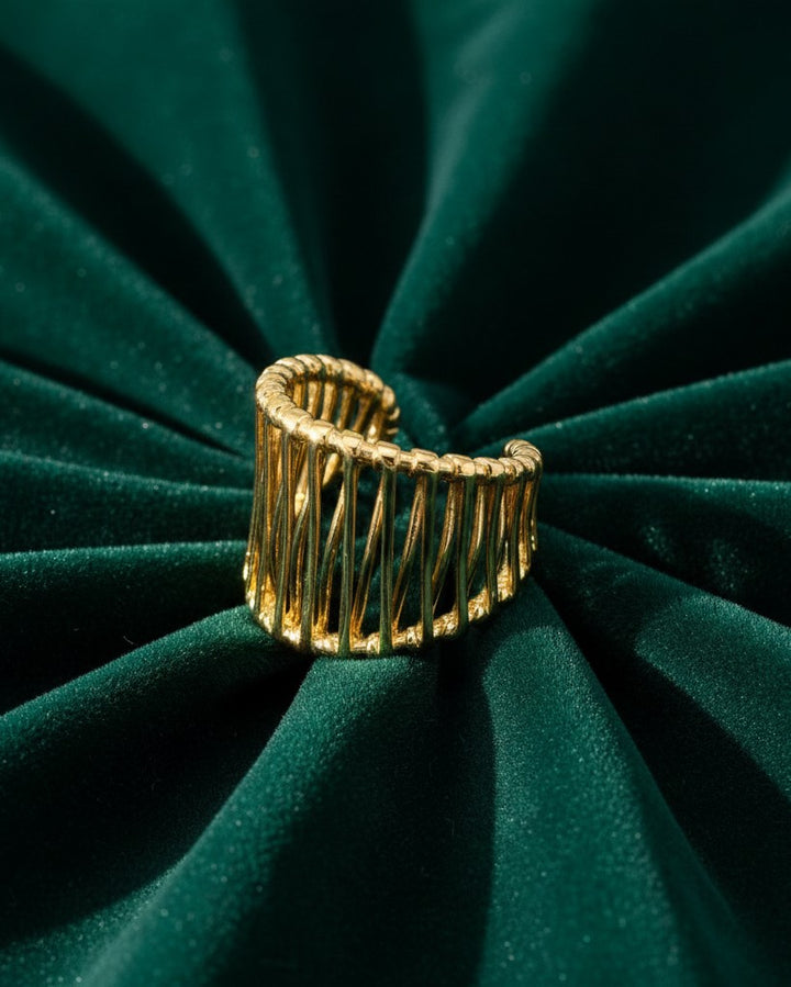 Elli Jewellery gold plated hollow geometric statement ring with a vertical cage design on dark green velvet fabric.