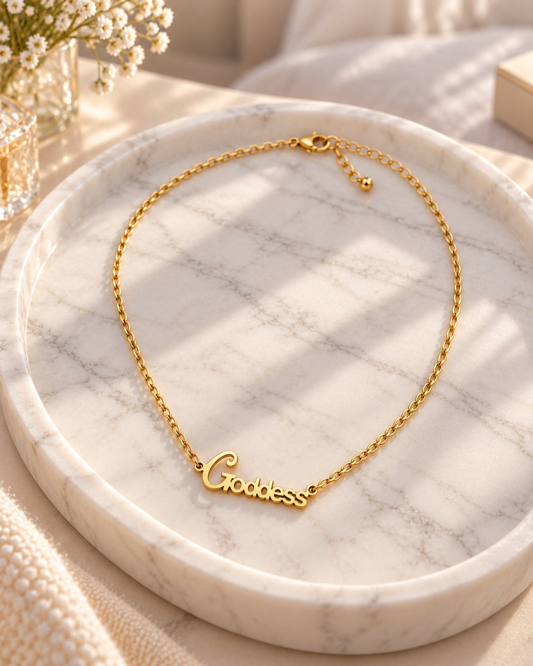 Elli Jewellery gold plated goddess pendant necklace on a marble tray with soft sunlight.