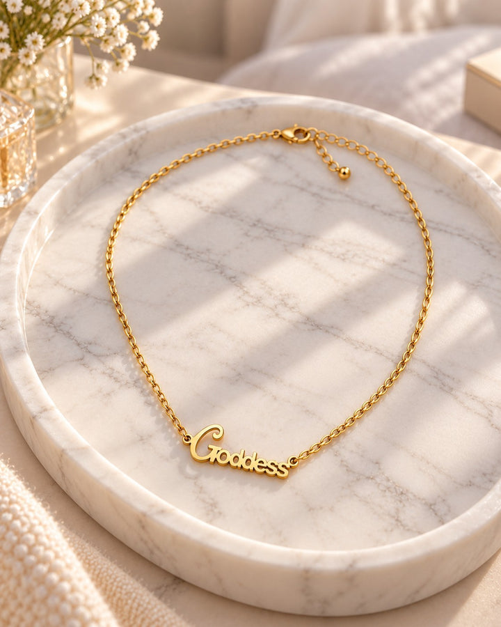 Elli Jewellery gold plated goddess pendant necklace on a marble tray with soft sunlight.