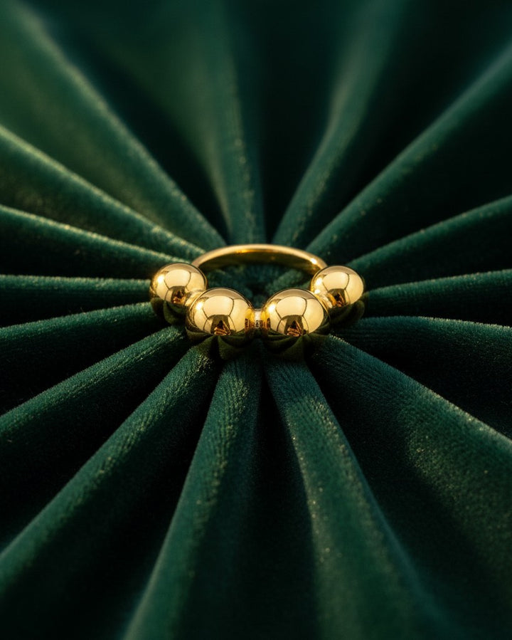 Elli Jewellery gold plated statement ring featuring a row of graduated polished spheres on a dark green velvet background