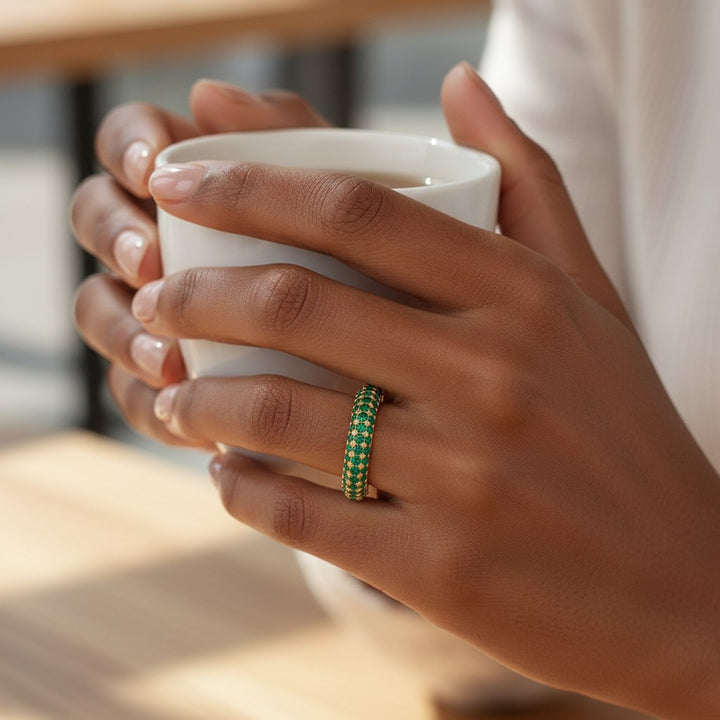 Elli Jewellery gold plated pavé ring with green crystals worn on a finger while holding a white coffee cup