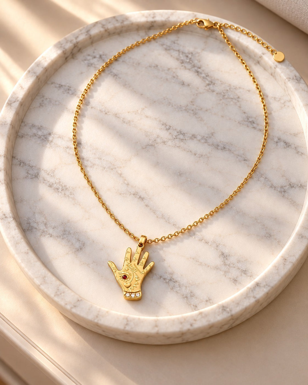 Elli Jewellery gold plated hamsa hand pendant necklace with evil eye detail on a marble tray