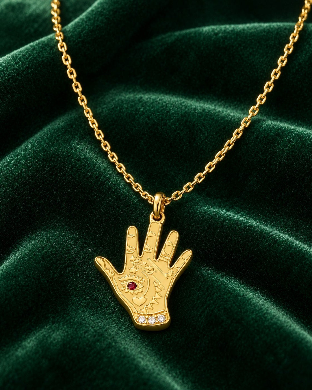 Elli Jewellery gold plated hamsa hand pendant necklace with evil eye detail on a dark green velvet background