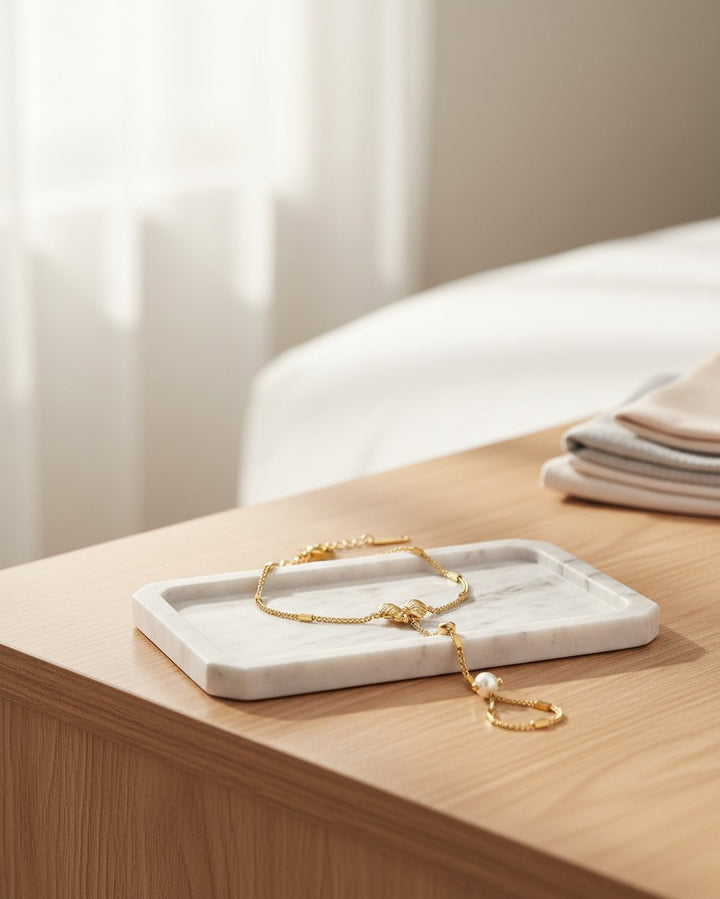 Elli Jewellery gold plated hand chain bracelet with attached ring and pearl detail resting on a white marble tray.