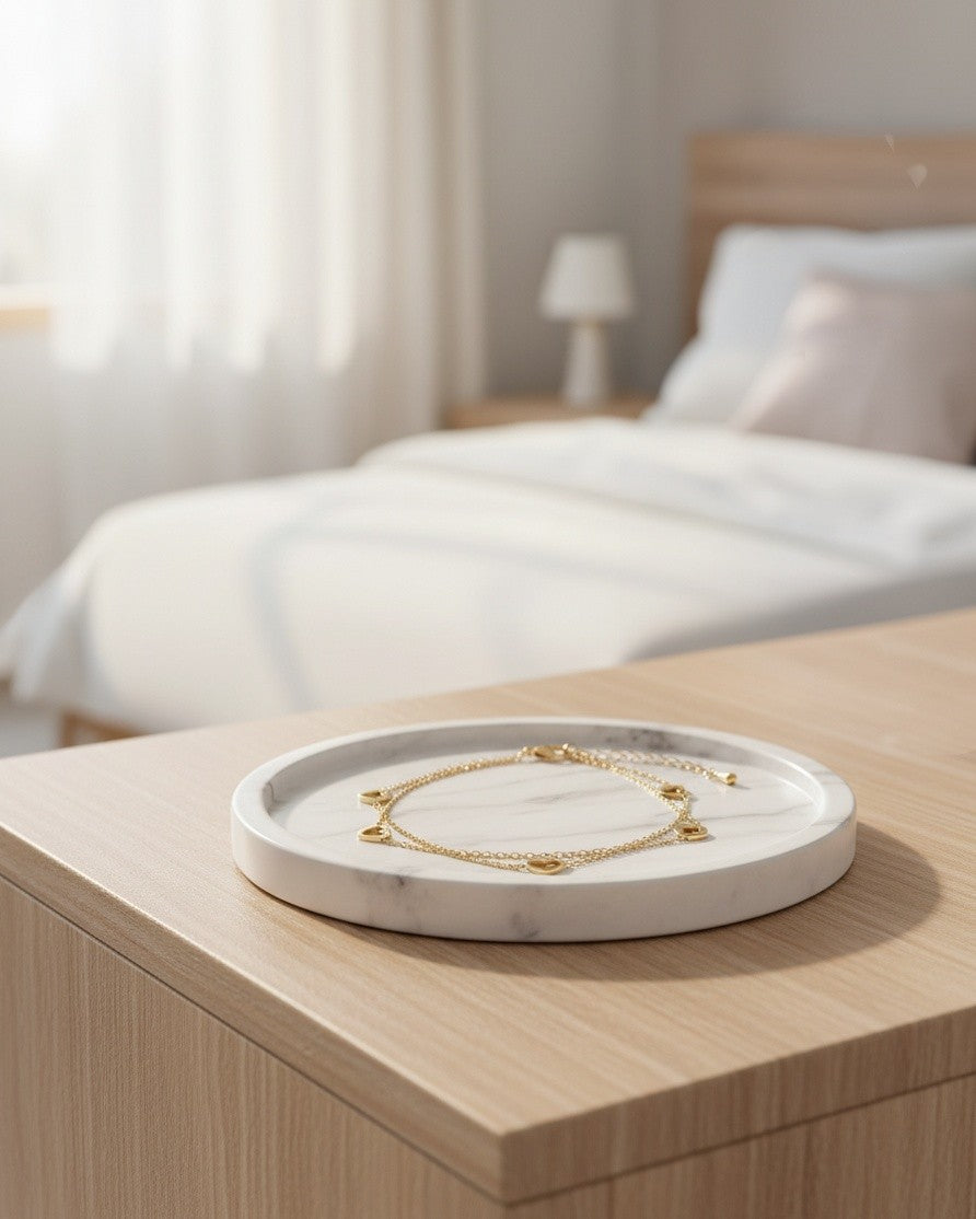 Elli Jewellery gold-toned heart charm anklet resting on a white marble tray in a bright bedroom setting.