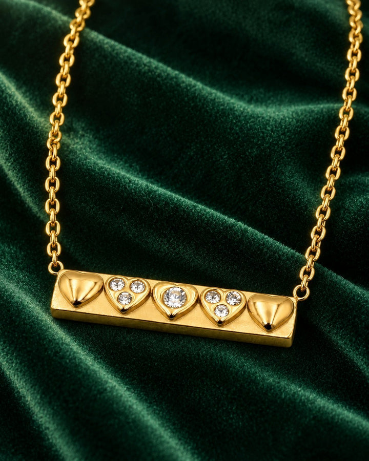 Elli Jewellery gold plated bar necklace featuring three heart charms and two sparkling crystals on green velvet