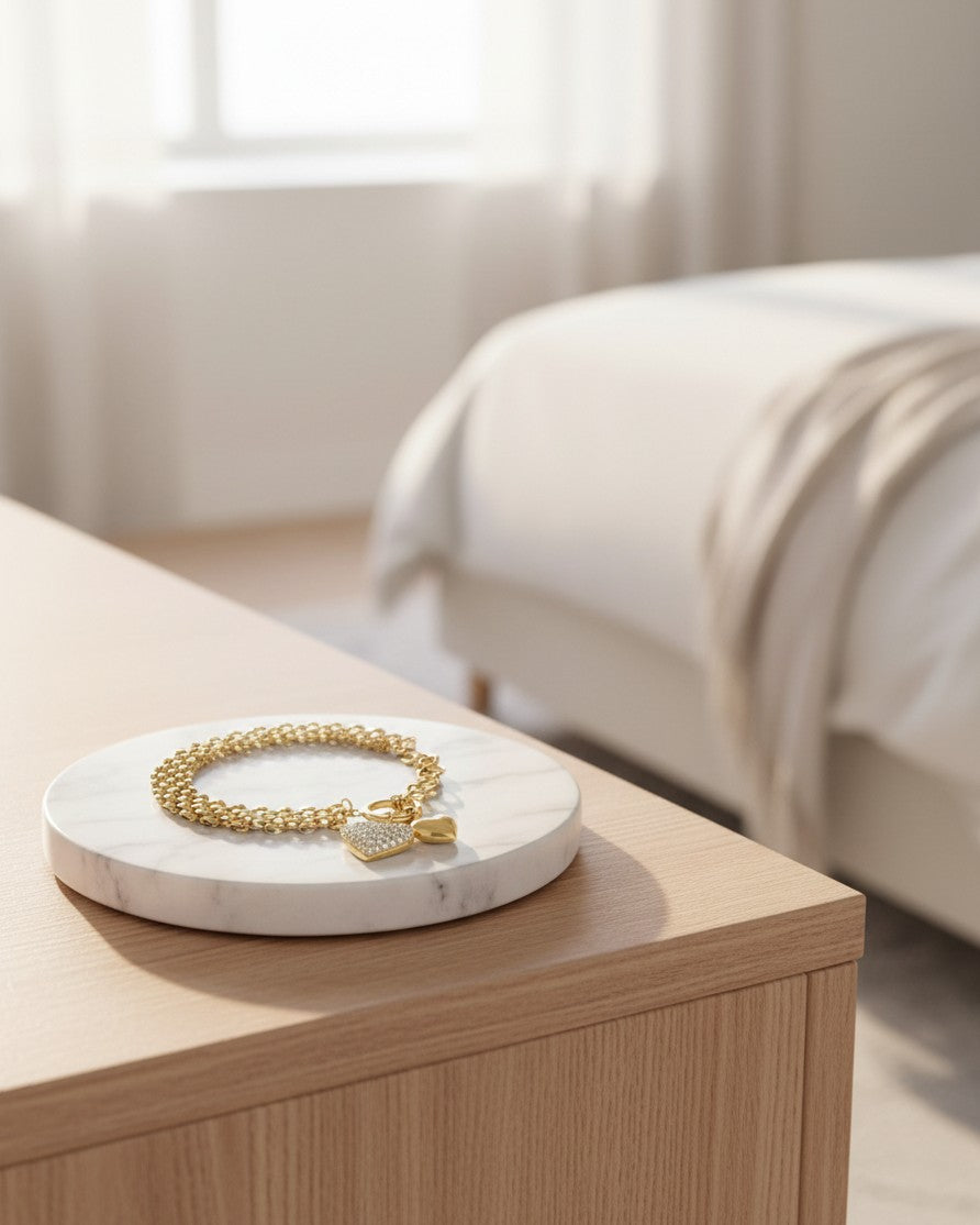 Elli Jewellery gold plated heart charm chain bracelet resting on a white marble display stand in a bedroom setting.