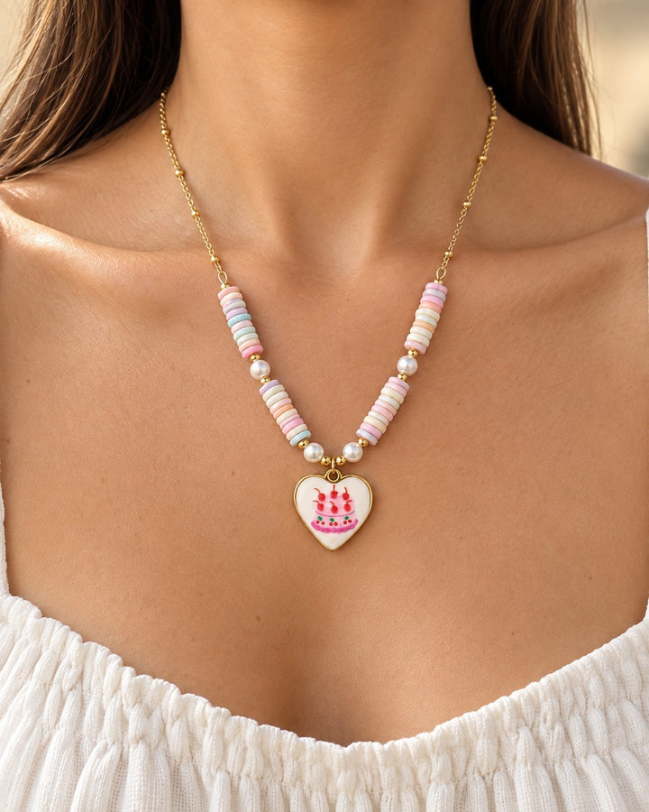 Elli Jewellery gold plated necklace featuring a white heart charm with cake design and pastel beaded chain on a model