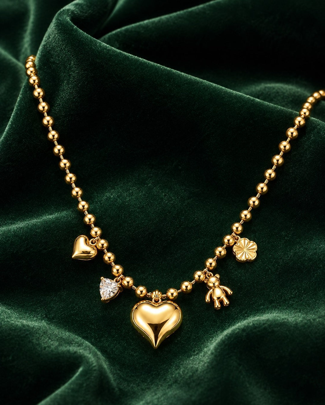 Elli Jewellery gold plated beaded chain necklace featuring heart, teddy bear, and crystal charms on green velvet.