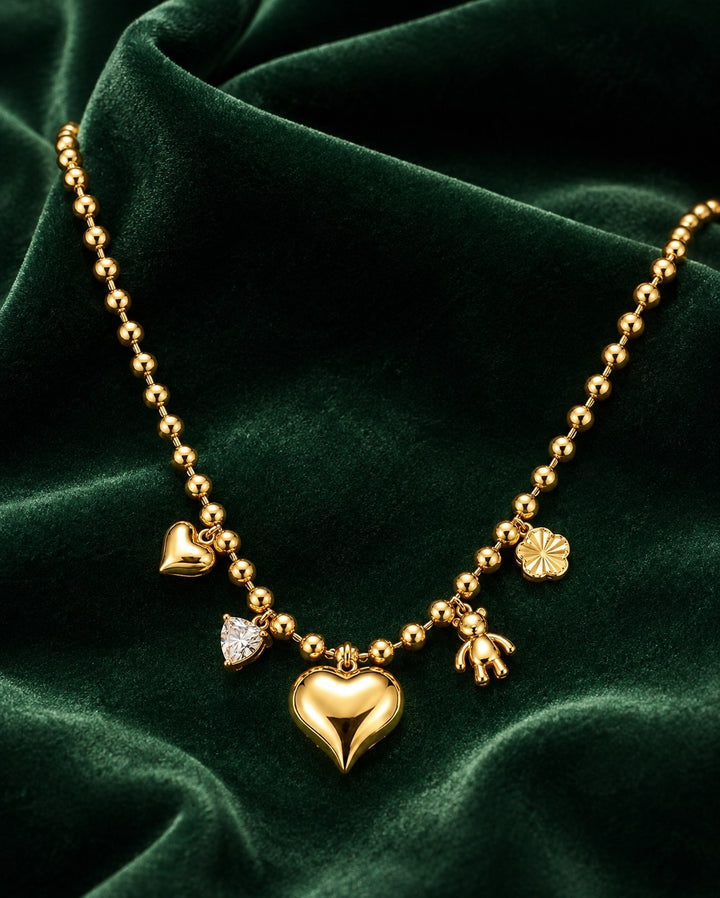 Elli Jewellery gold plated beaded chain necklace featuring heart, teddy bear, and crystal charms on green velvet.