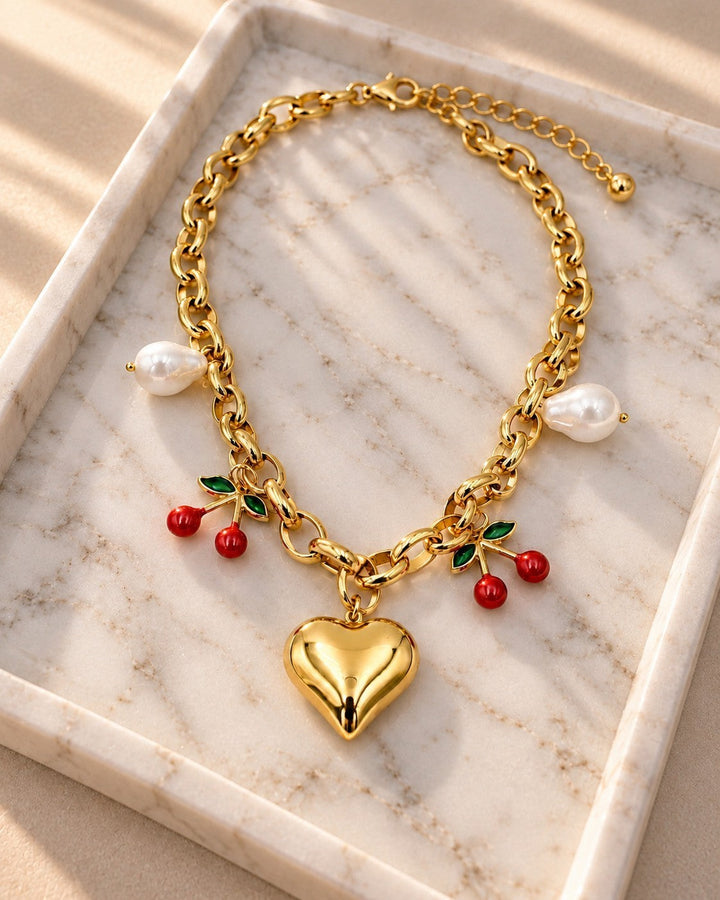 Elli Jewellery gold plated chain necklace featuring a heart charm, cherry charms, and pearl accents on a marble tray.