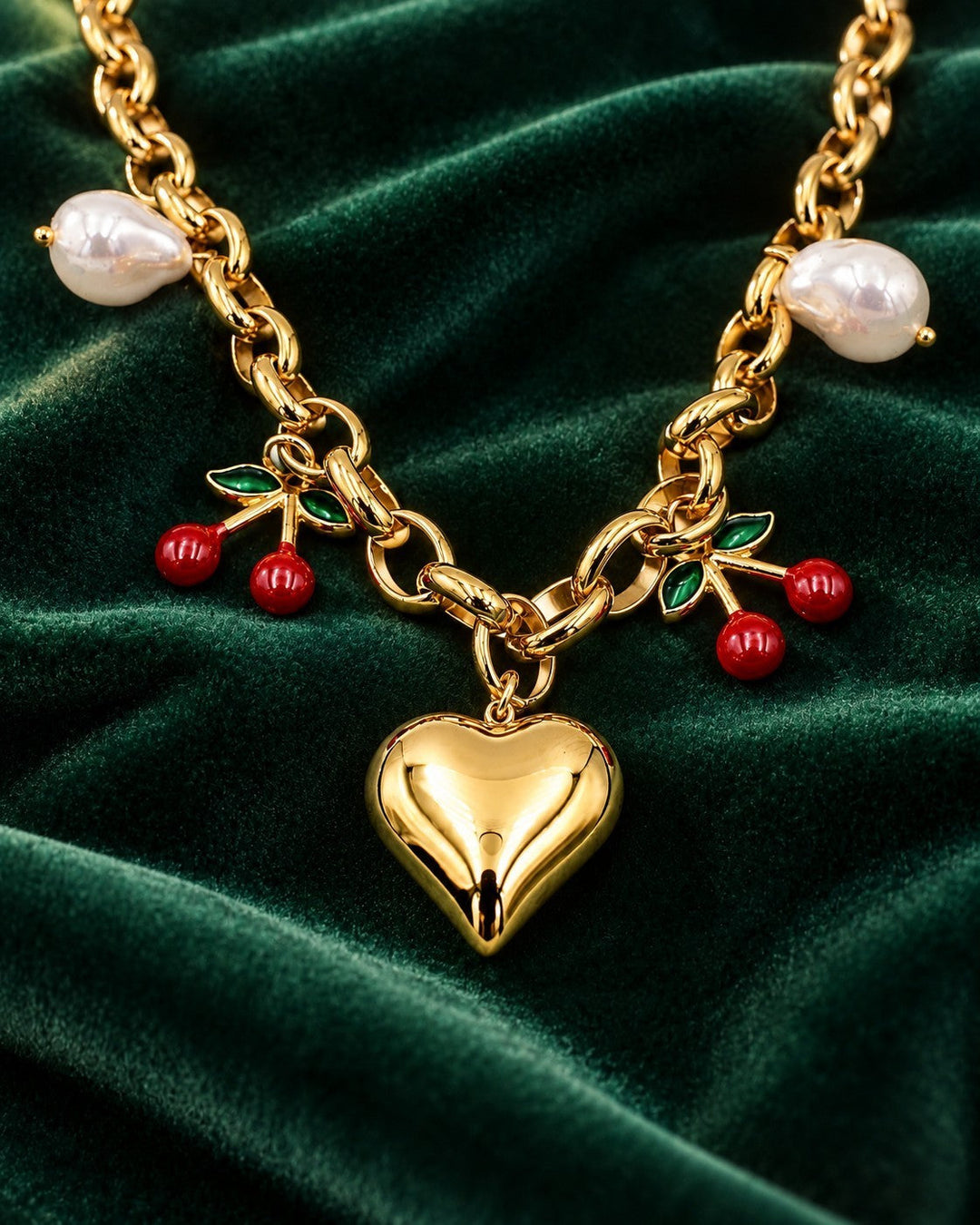 Elli Jewellery gold plated necklace featuring a heart charm, cherry charms, and white pearls on a green velvet cloth.