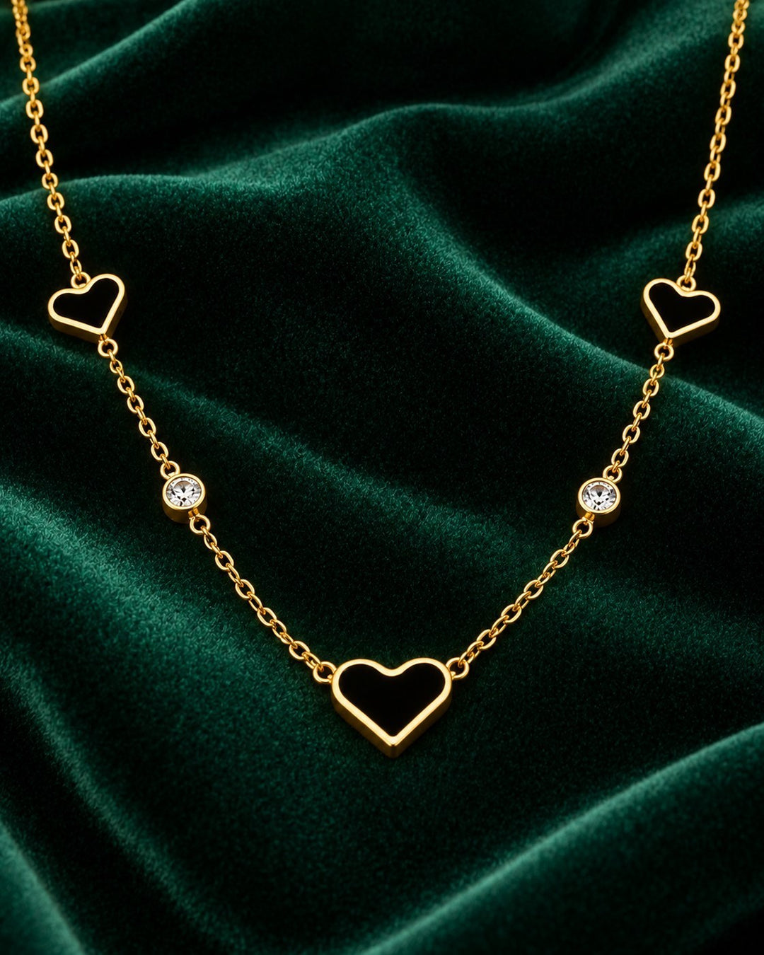 Elli Jewellery gold plated necklace featuring darkened heart pendants and sparkling crystals on a green velvet background