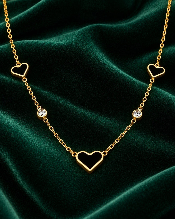 Elli Jewellery gold plated necklace featuring darkened heart pendants and sparkling crystals on a green velvet background