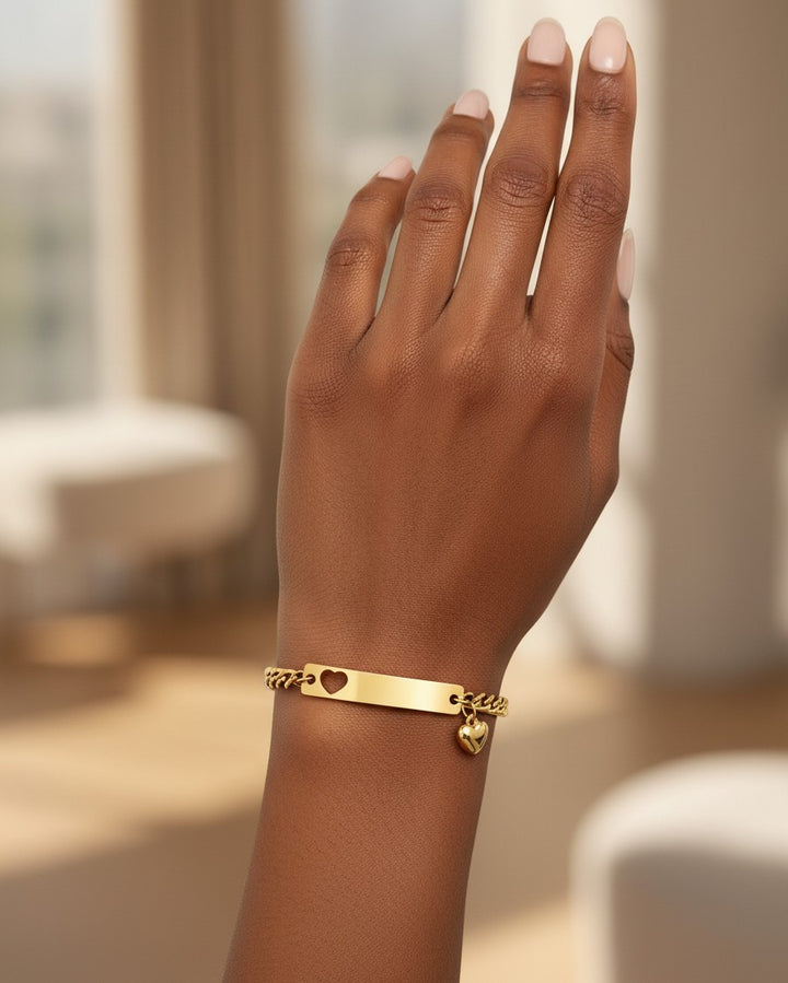 Elli Jewellery gold plated waterproof ID bracelet with a heart cutout and charm worn on a model's wrist
