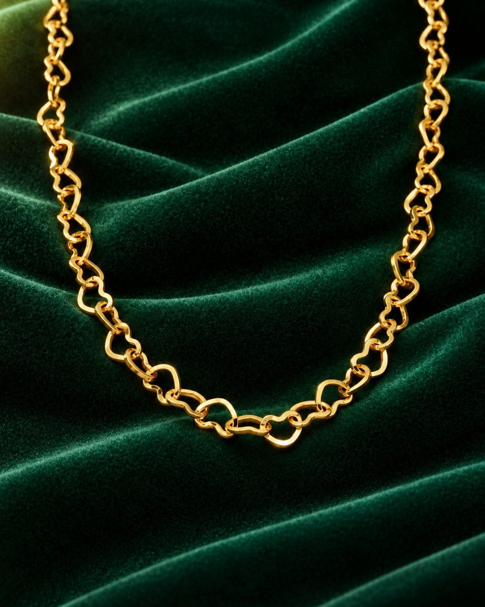 Elli Jewellery gold plated dainty heart link choker necklace resting on a luxurious dark green velvet background.