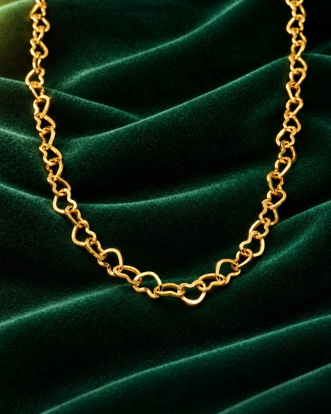 Elli Jewellery gold plated dainty heart link choker necklace resting on a luxurious dark green velvet background.