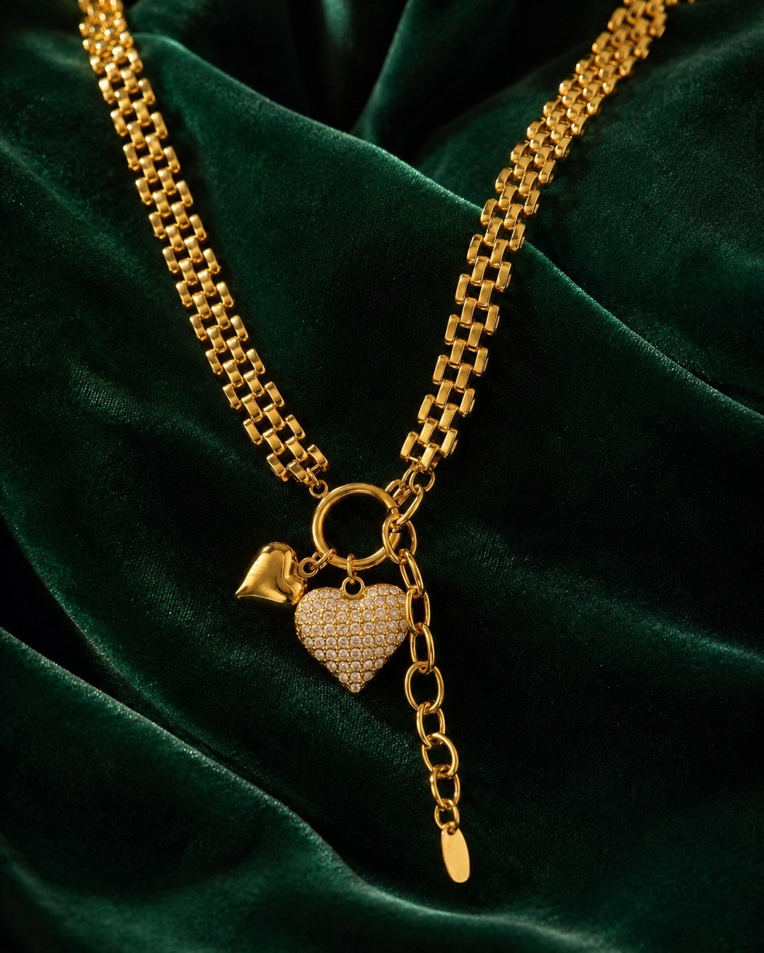 Elli Jewellery gold plated waterproof heart charm necklace with crystal accents on a dark green velvet background