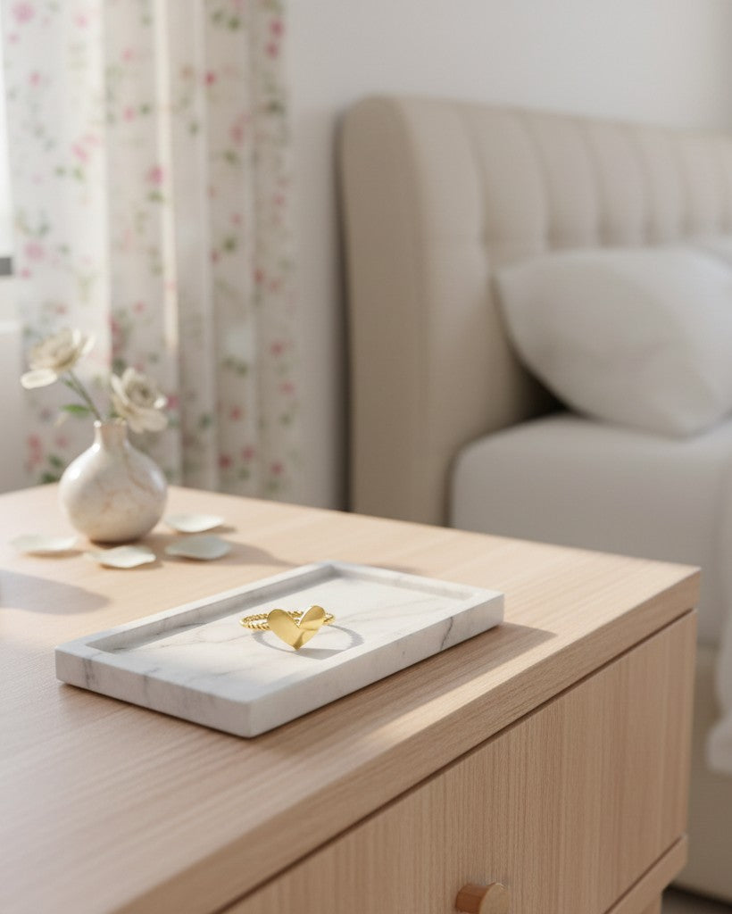 Elli Jewellery gold plated heart ring with a twisted rope band resting on a white marble tray in a bedroom.