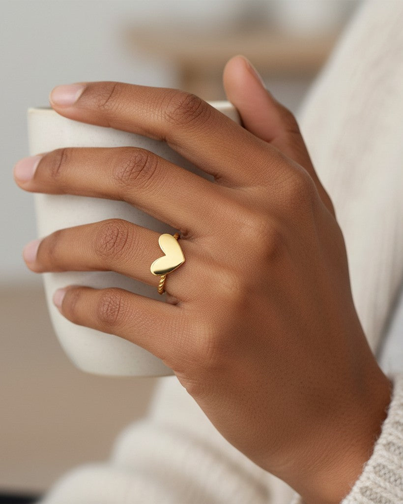 Elli Jewellery gold plated heart ring with a twisted rope band worn on a finger while holding a ceramic mug