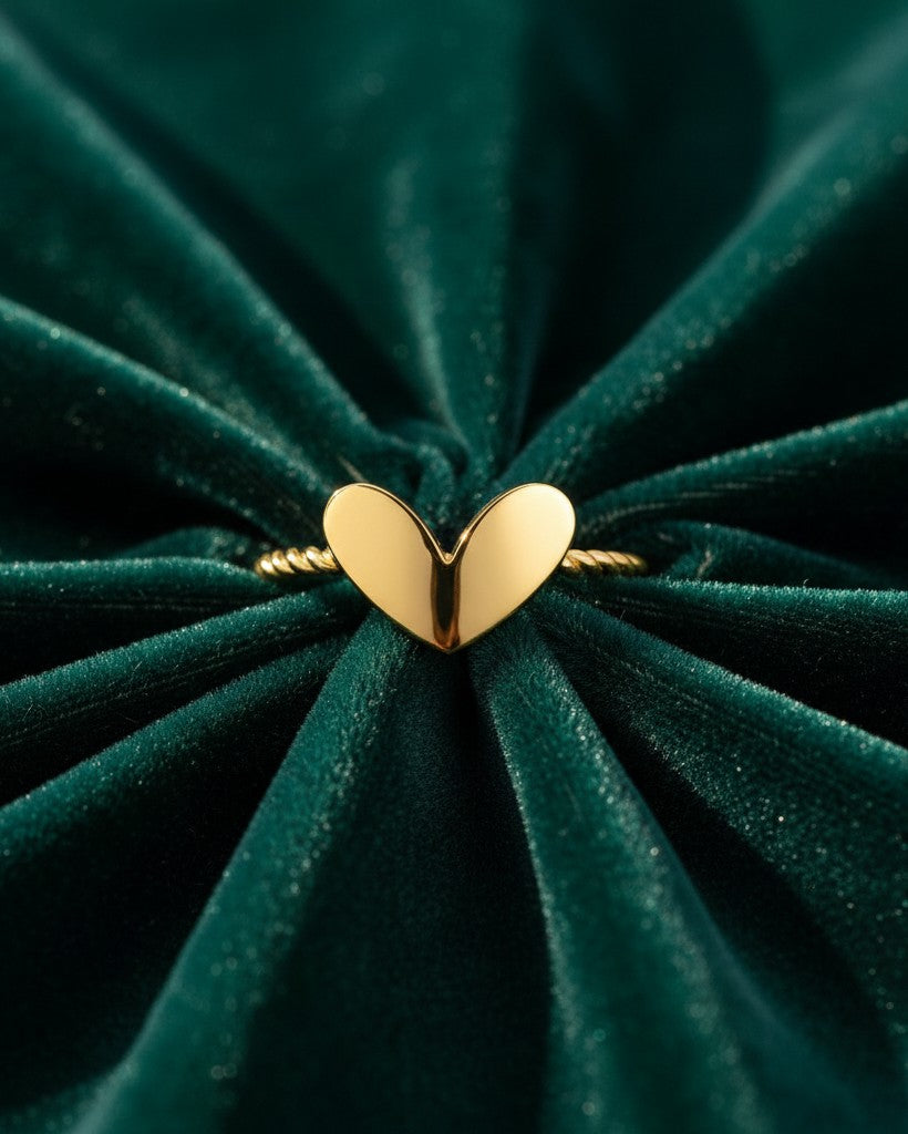 Elli Jewellery gold plated heart ring with a twisted rope band resting on dark green velvet fabric.