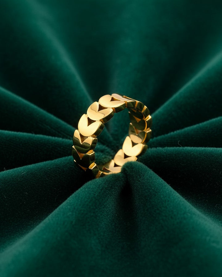 Elli Jewellery gold plated stacking ring featuring a delicate repeating heart pattern on a dark green velvet background