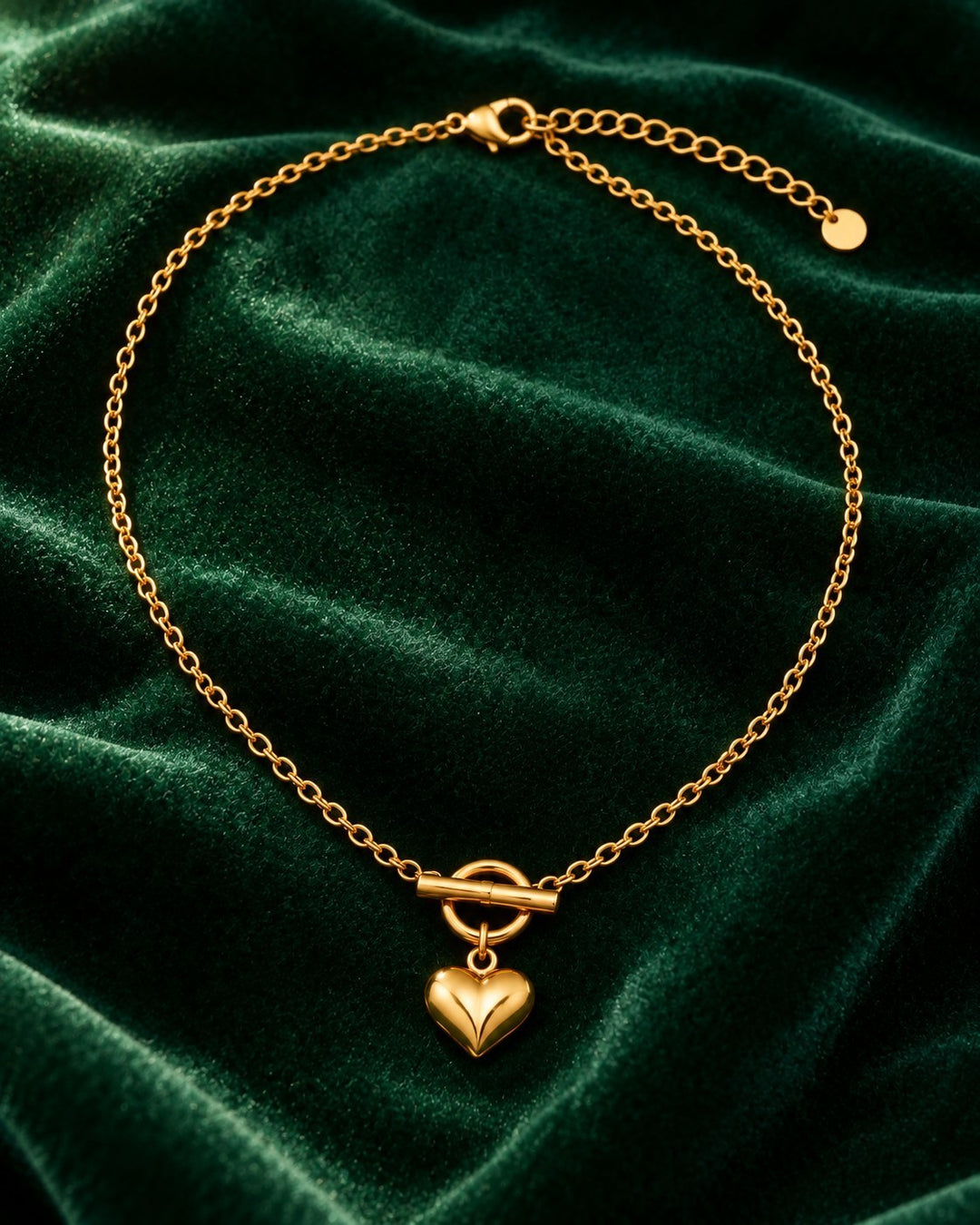 Elli Jewellery gold plated heart pendant necklace with a toggle clasp on a dark green velvet background.