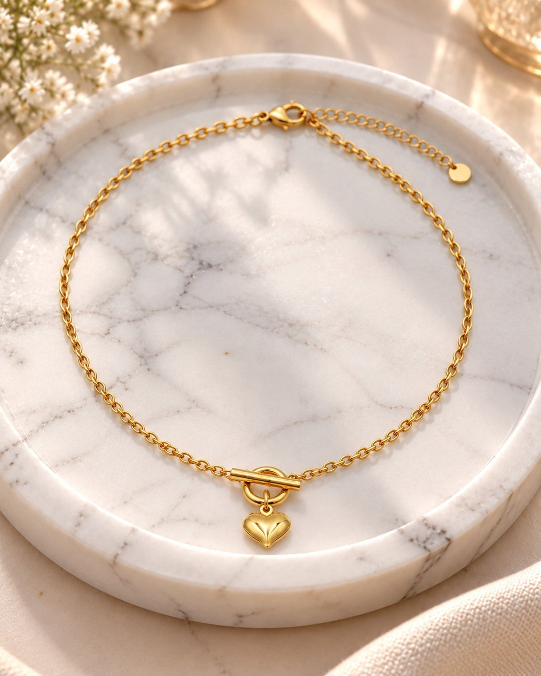 Elli Jewellery gold plated heart pendant necklace featuring a sleek chain and toggle clasp on a marble tray.