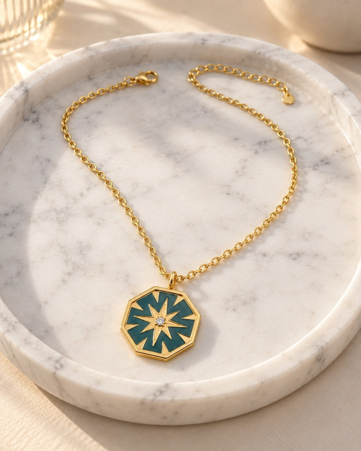 Elli Jewellery gold plated hexagon pendant necklace with mint green enamel and a central star detail on a marble tray
