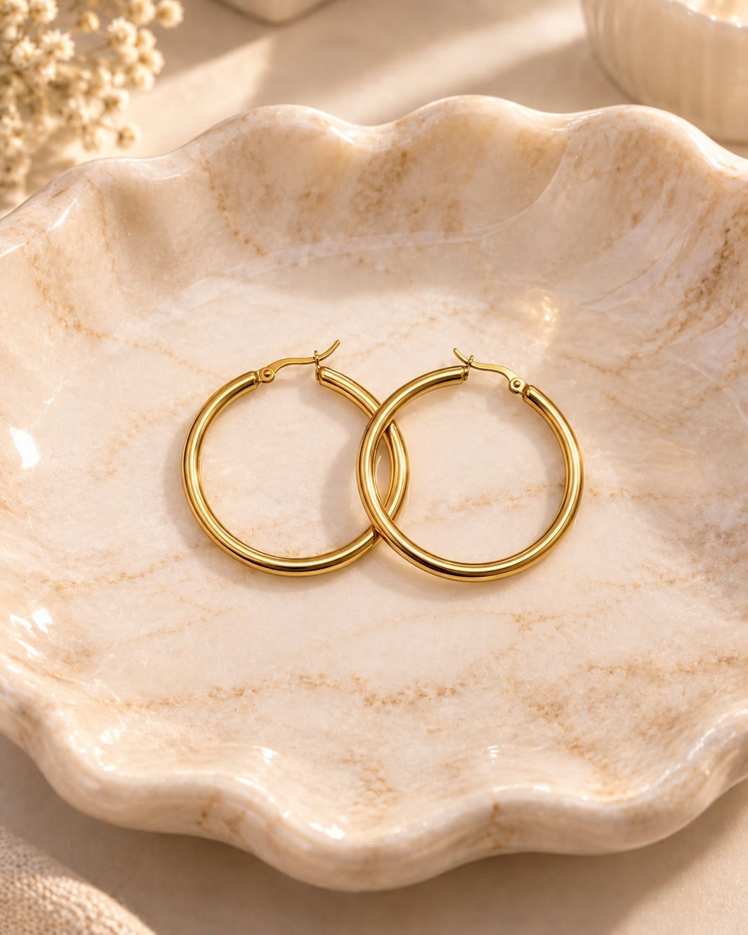 Elli Jewellery gold-toned 40mm hoop earrings resting in a decorative scalloped marble dish.