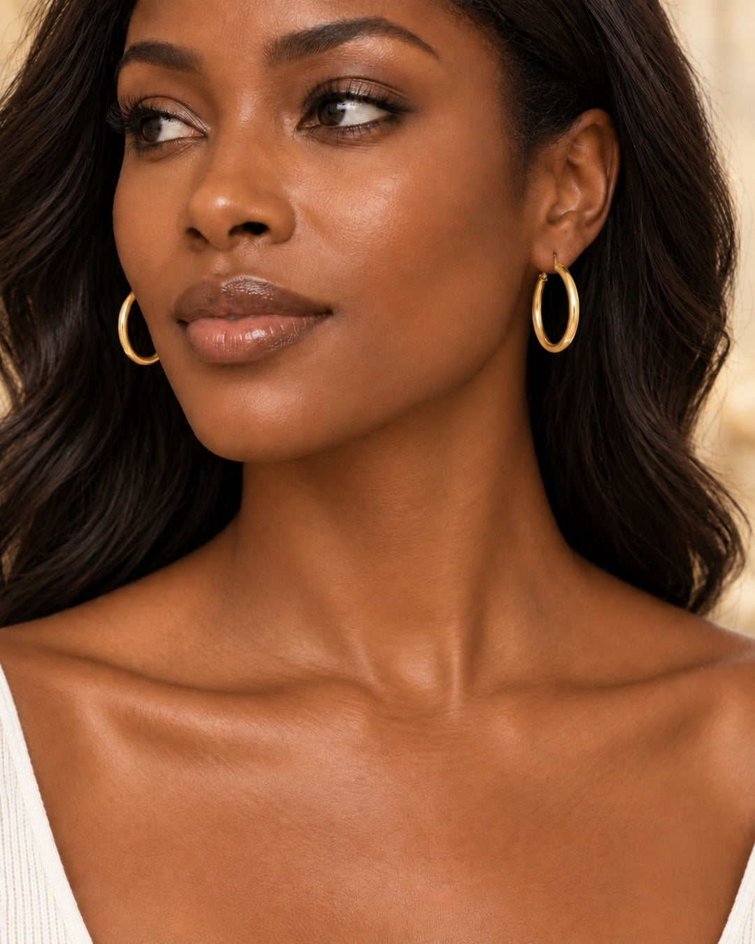 Elli Jewellery 40mm gold-toned hoop earrings worn by a woman with long dark wavy hair