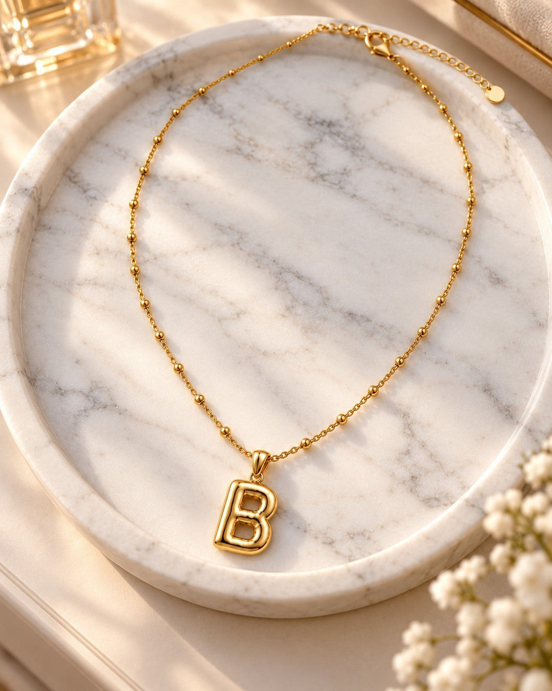 Elli Jewellery gold plated chunky initial B pendant necklace with a delicate beaded chain on a marble tray.