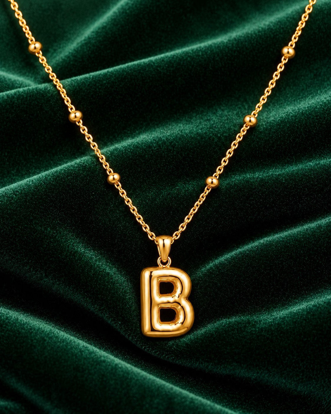 Elli Jewellery gold plated chunky initial B pendant necklace on a dark green velvet background