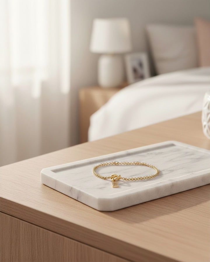 Elli Jewellery gold plated waterproof chain bracelet with a sparkling diamanté letter E charm on a marble tray.