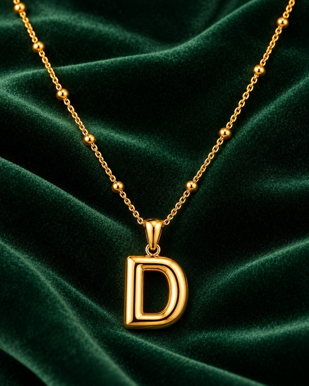 Elli Jewellery gold plated chunky initial D letter pendant necklace on a dark green velvet background