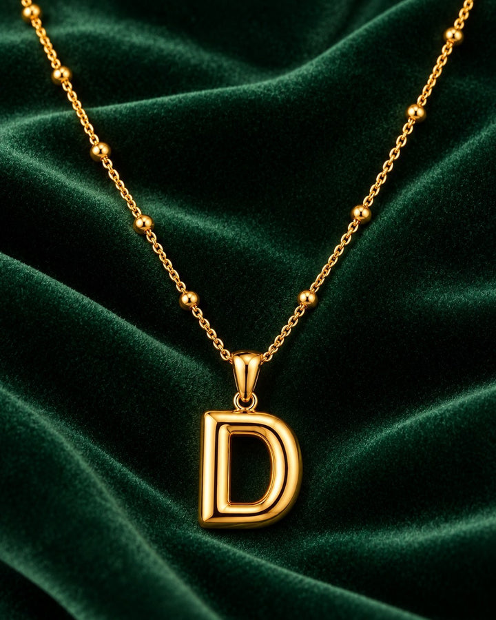 Elli Jewellery gold plated chunky initial D letter pendant necklace on a dark green velvet background