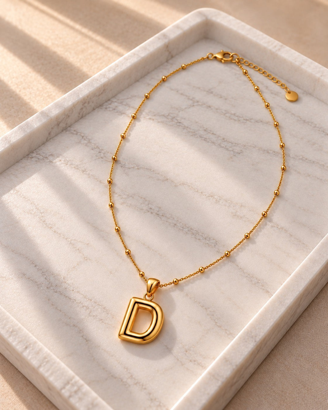 Elli Jewellery gold plated chunky initial D pendant necklace on a marble tray with delicate beaded chain detail.