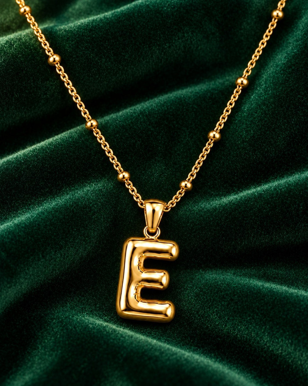 Elli Jewellery gold plated chunky initial E pendant necklace on a dark green velvet background