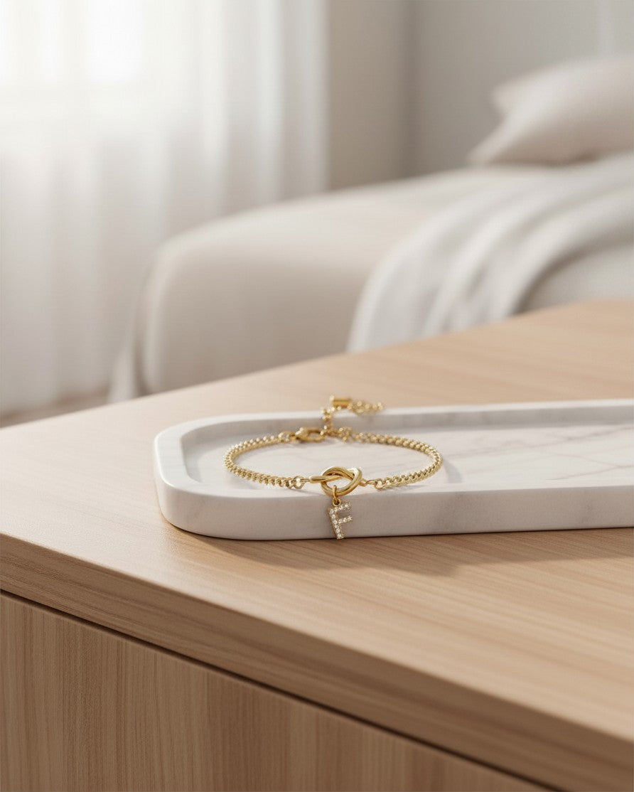Elli Jewellery gold plated waterproof charm bracelet featuring a sparkling diamante initial F on a marble tray