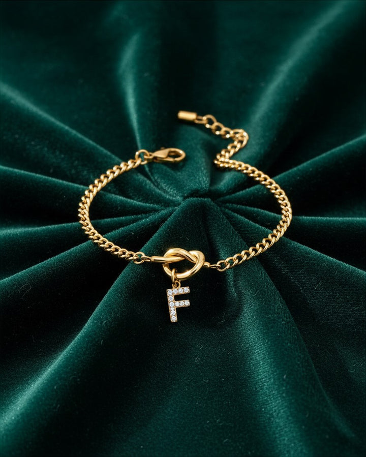 Elli Jewellery gold plated chain bracelet featuring a sparkling diamante initial F charm on a dark green velvet cloth.