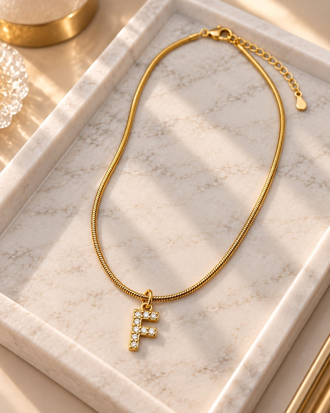 Elli Jewellery gold plated waterproof initial F pendant necklace with crystal accents on a marble tray