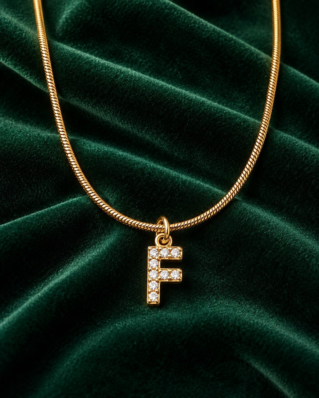 Elli Jewellery gold plated waterproof initial F pendant necklace with clear stones on a dark green velvet background