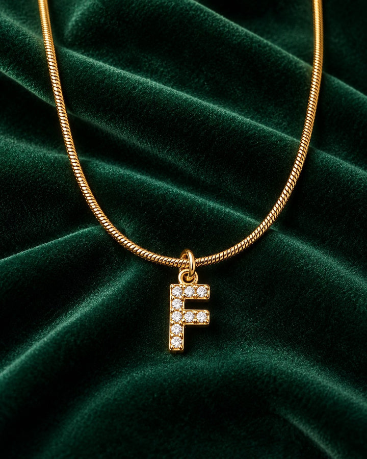Elli Jewellery gold plated waterproof initial F pendant necklace with clear stones on a dark green velvet background
