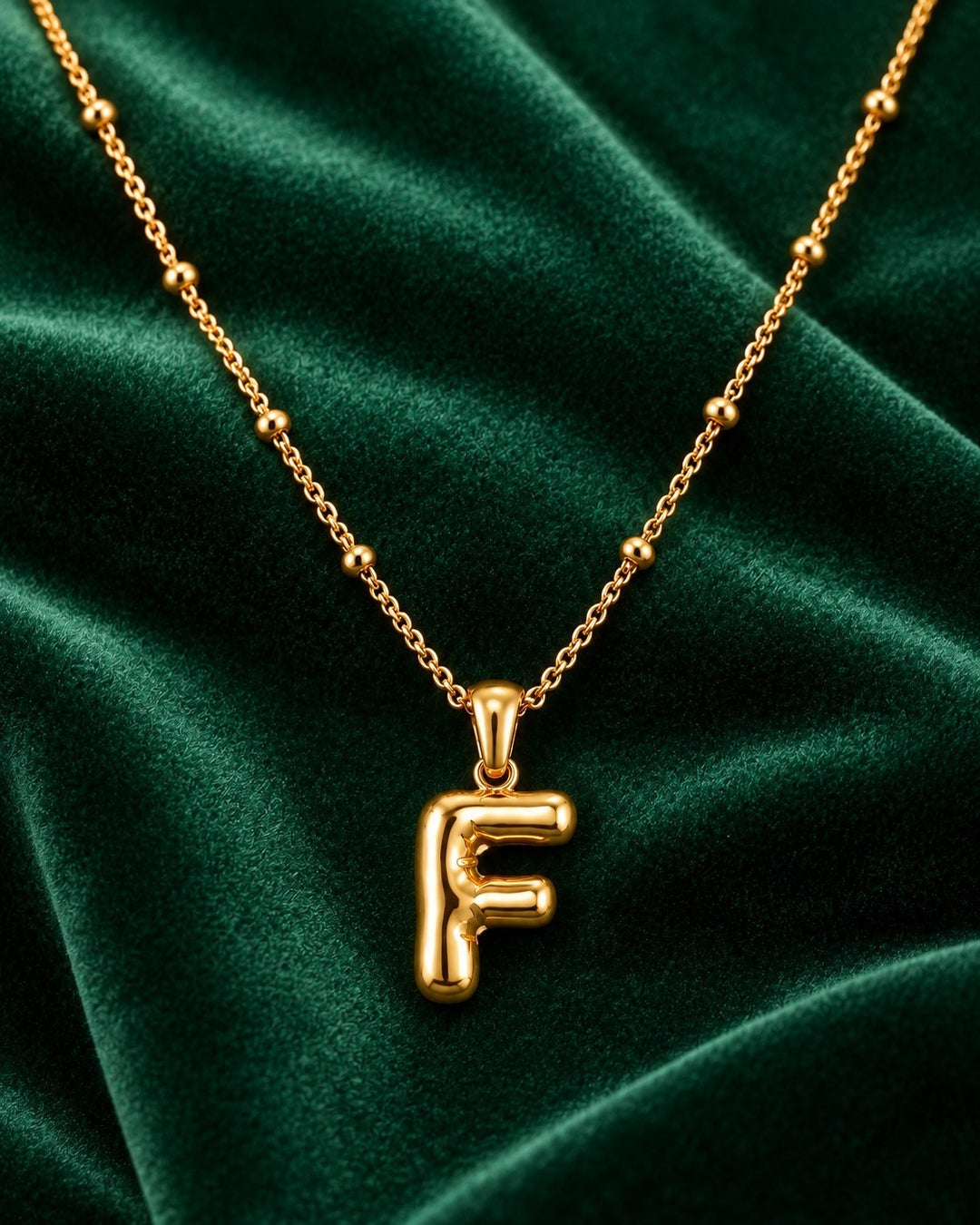 Elli Jewellery gold plated chunky initial F pendant necklace on a dark green velvet background